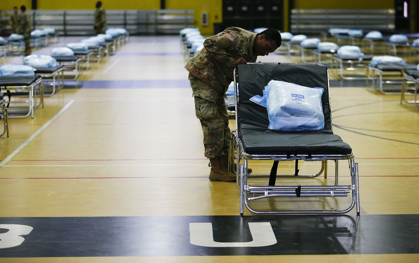 a member of the national guard sets up a hopital bed in a gymnasium