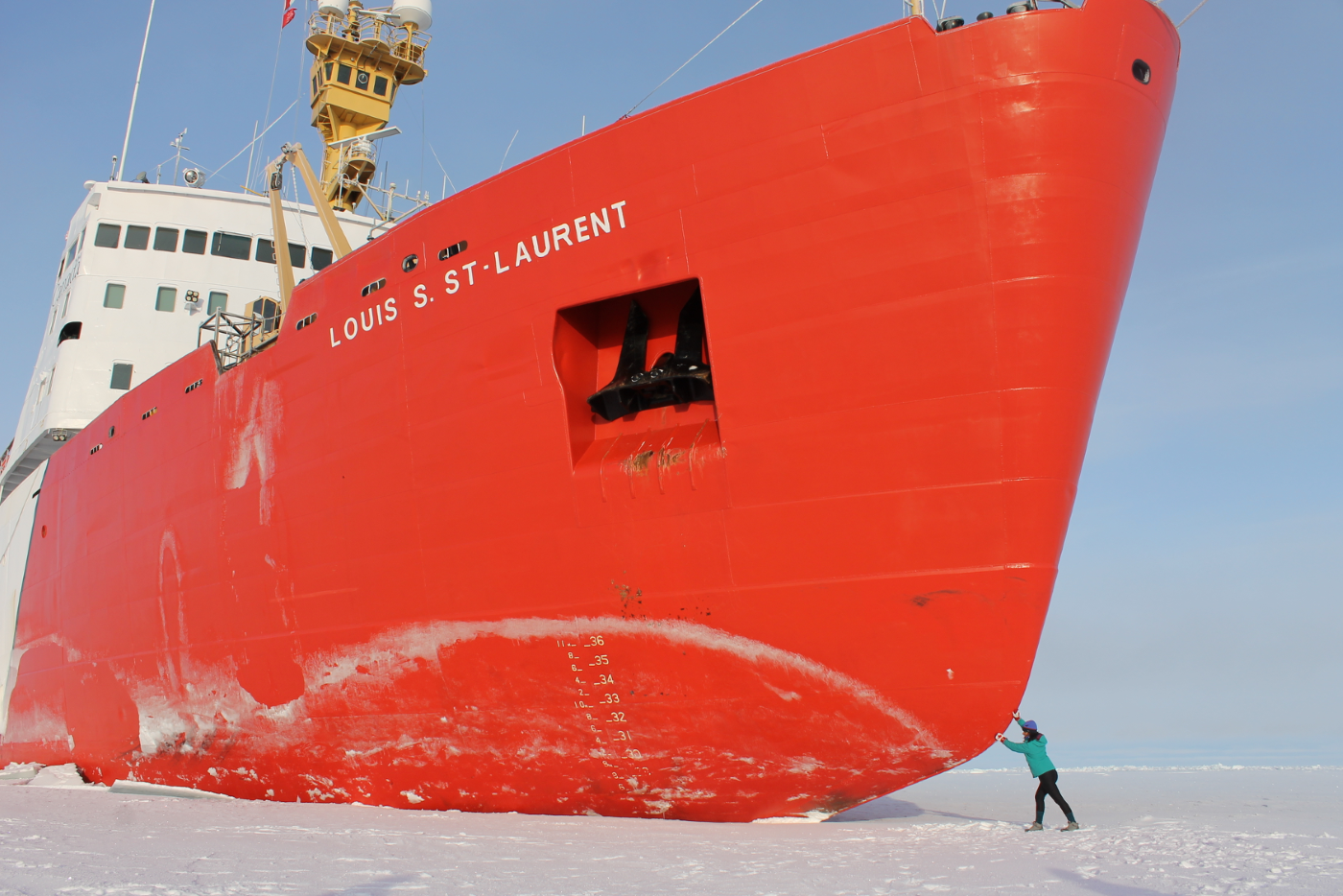 Large red  ice breaker ship fills the frame with small figure in the bottom right seeming to push the ship