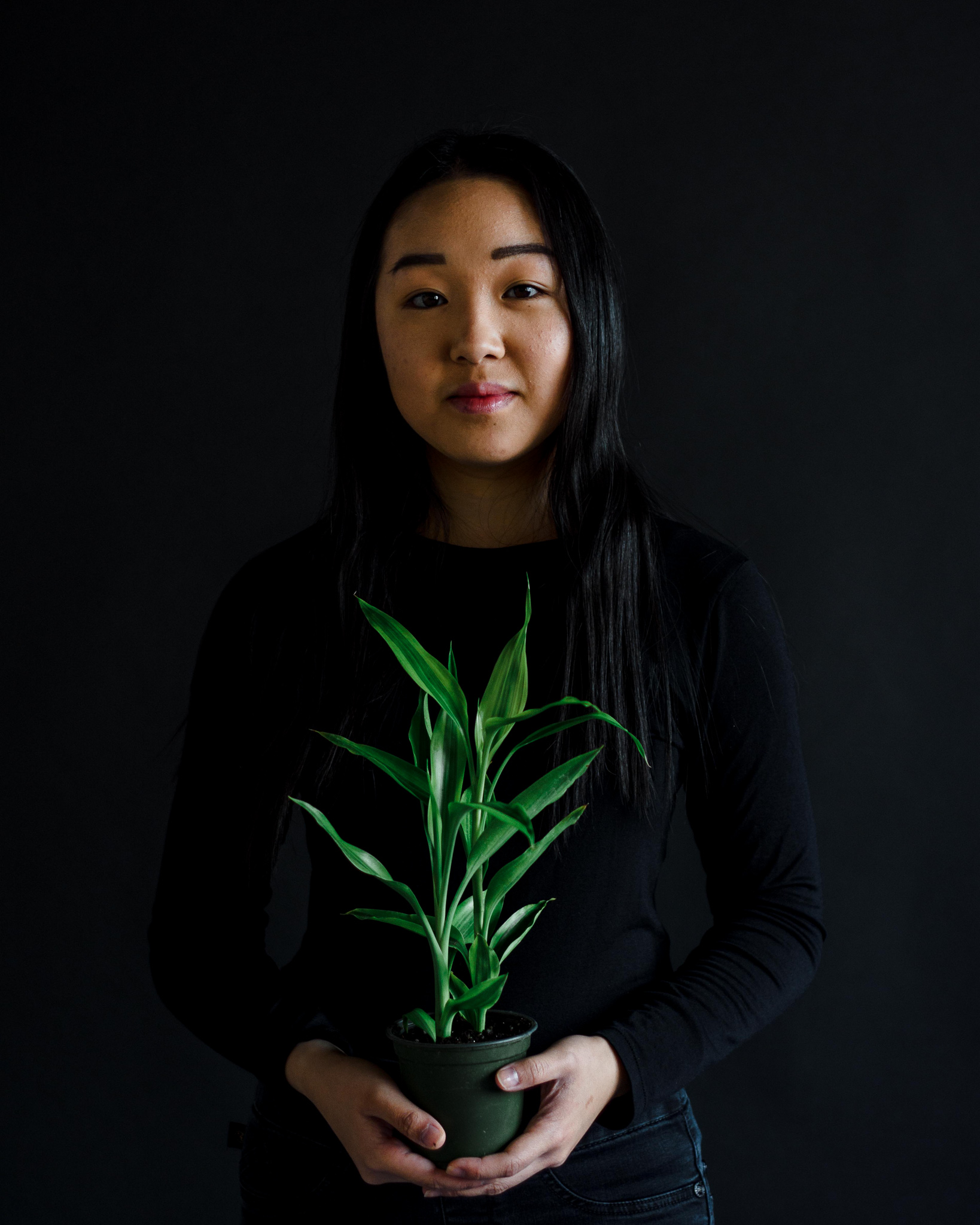 Portrait of Jess Lin holding a plant, in front of a dark field