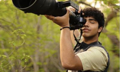Aman Sharma holds a camera with a long lens surrounded by nature.